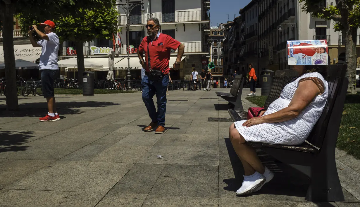 Seorang wanita melindungi kepalanya di bawah majalah di Alun-Alun Plaza del Castillo, Pamplona, Spanyol, 15 Juni 2022. Layanan cuaca Spanyol mengatakan massa udara panas dari Afrika Utara memicu gelombang panas besar pertama di negara itu tahun ini dengan suhu diperkirakan akan meningkat menjadi 43 derajat Celcius (109 derajat Fahrenheit) di area tertentu. (AP Photo/Alvaro Barrientos)