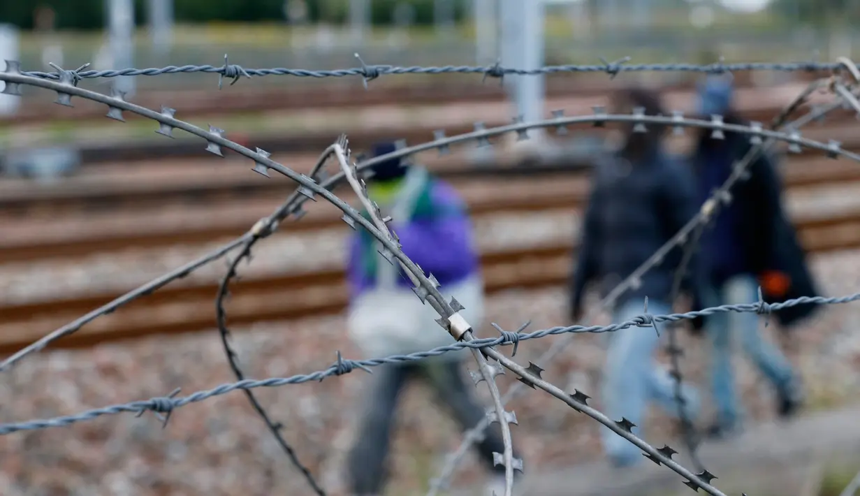 Sejumlah imigran terlihat dari balik pagar berduri sedang berjalan dekat rel kereta di Coquelles dekat Calais di Prancis, 29 Juli 2015. Ribuan imigran tersebut mencoba memasuki Terowongan Channel menuju Inggris melalui Prancis. (REUTERS/Pascal Rossignol)