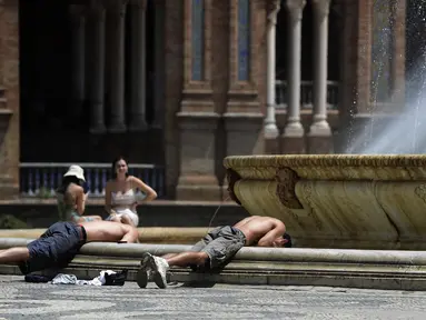 Dua pemuda membenamkan kepala mereka ke dalam air mancur untuk mendinginkan diri, di alun-alun Plaza de Espana di Seville, Spanyol pada 7 Agustus 2023. (CRISTINA QUICLER / AFP)