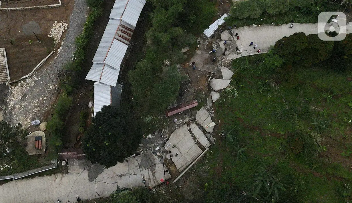Foto udara kondisi jalan yang terbelah akibat pergeseran tanah di kawasan Bojong Koneng, Babakan Madang, Kabupaten Bogor, Jawa Barat, Jumat (16/9/2022). Badan Penanggulangan Bencana Daerah (BPBD) setempat mencatat 18 unit rumah mengalami kerusakan, dan pergeseran tanah itu menyebabkan retakan-retakan di tanah, dinding, plafon dan lantai rumah warga serta akses jalan sudah tidak bisa dilewati oleh kendaraan roda dua dan roda empat. (Liputan6.com/Herman Zakharia)