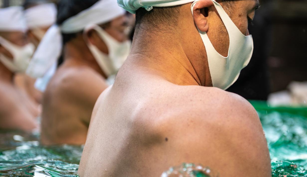 Penganut Shinto dari Kuil Teppozu Inari mandi dengan air dingin untuk mensucikan jiwa dan tubuh mereka selama ritual Tahun Baru di Tokyo, Jepang, Minggu (9/1/2022). Ritual tahunan mandi air dingin ini bertujuan mengharapkan kesehatan serta keberuntungan di tahun yang baru. (Philip FONG/AFP)