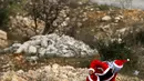 Seorang demonstran Palestina mengenakan kostum Santa Claus melempar batu ke arah pasukan keamanan Israel saat terjadi bentrokan di pos pemeriksaan Atarot di pinggiran utara Yerusalem (19/12). (AFP Photo/Abbas Momani)