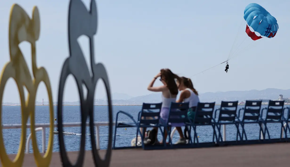 Wisatawan menikmati suasana pantai di dekat ornamen Tour De France 2020 di kota Nice, French Riviera, Rabu (26/8/2020). Ajang balap sepeda lintas kota di Prancis kali ini akan dimulai dari kota Nice pada 29 Agustus hingga 20 September di tengah kehawatiran COVID-19. (Kenzo Tribouillard/AFP)