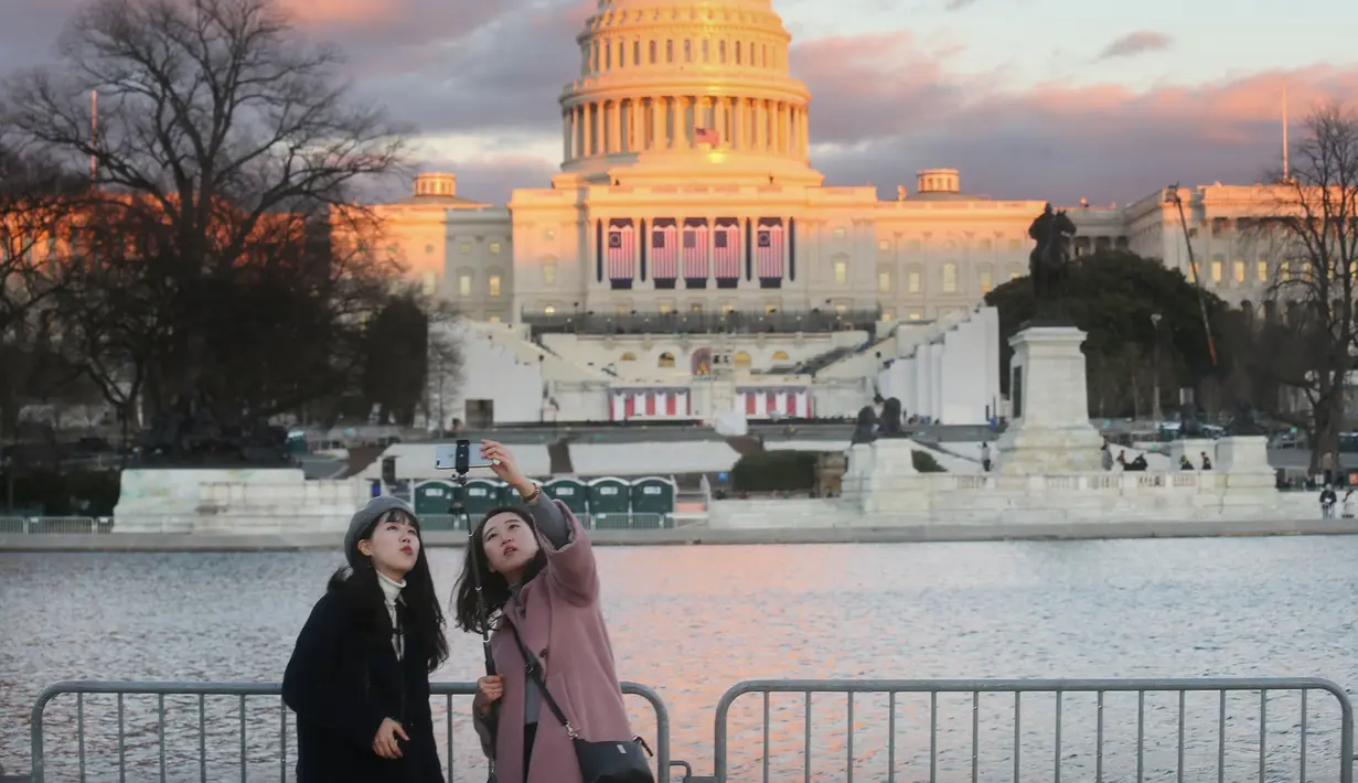 Dua orang wanita mengambil gambar dengan latar belakang Gedung Capitol, Washington DC yang merupakan tempat pelantikan Donald Trump dan Mike Pence sebagai presiden dan wakil presiden AS, Kamis (19/1). (Mario Tama/Getty Images/AFP)