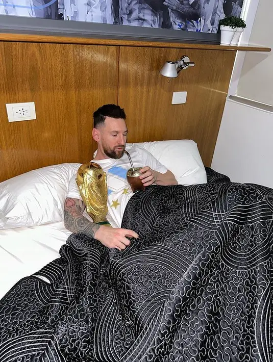 Kapten dan penyerang Argentina Lionel Messi menikmati minuman sambil memeluk trofi Piala Dunia 2022 di tempat tidur di pusat pelatihan AFA di Ezeiza, Buenos Aires, Argentina pada 20 Desember 2022. Trofi Piala Dunia merupakan satu-satunya gelar yang belum pernah diangkat pemain 35 tahun itu. Impiannya kini menjadi nyata trofi itu dipeluk sambil tidur. (Instagram/leomessi)