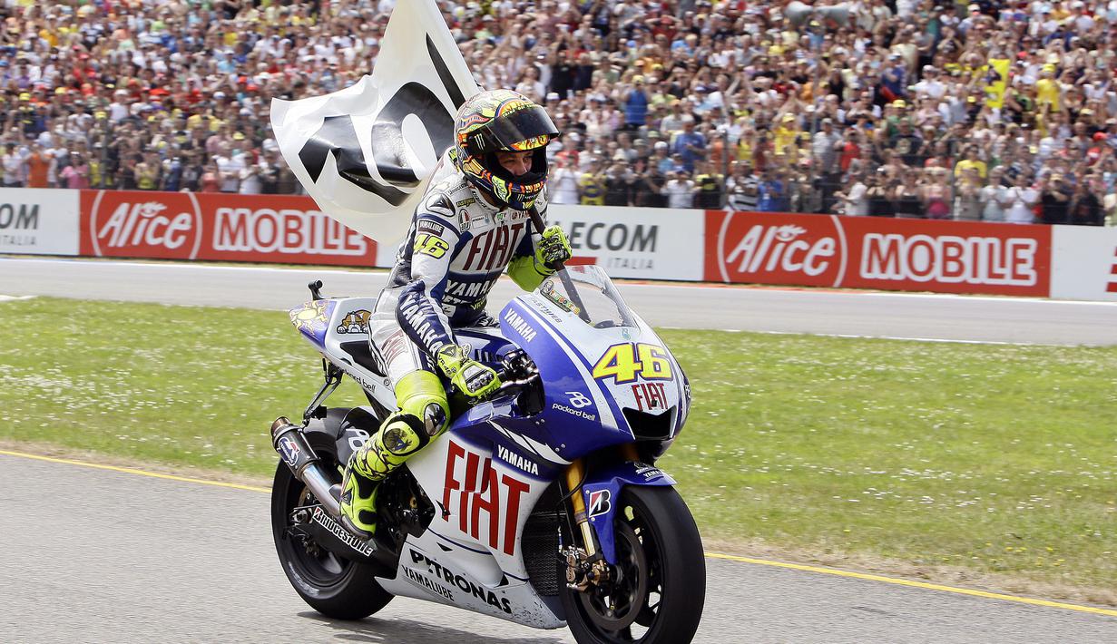 Valentino Rossi membawa bendera bertuliskan angka 100 ketika merayakan kemenangannya yang ke-100 dalam balapan MotoGP di sirkuit Assen pada Juni 2009. (AFP/ANP/Vincent Jannink)