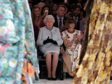 Ratu Elizabeth II duduk di sebelah Ratu Fashion, Anna Wintour menyaksikan pagelaran London Fashion Week 2018, Selasa (20/2). Ratu Elizabeth tampil stylish mengenakan setelan jaket dan rok biru muda keluaran Angela Kelly. (Yui Mok/Pool photo via AP)