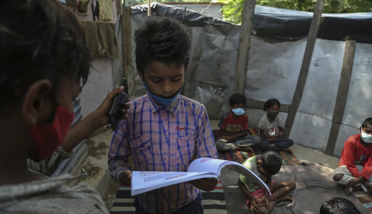Seorang siswa memegang ponsel untuk yang lain sehingga dia dapat mendengarkan instruksi dari seorang guru saat menghadiri kelas online di sebuah perkampungan kumuh di pinggiran Jammu, India, Senin, 14 Juni 2021.  (AP Photo/Channi Anand)