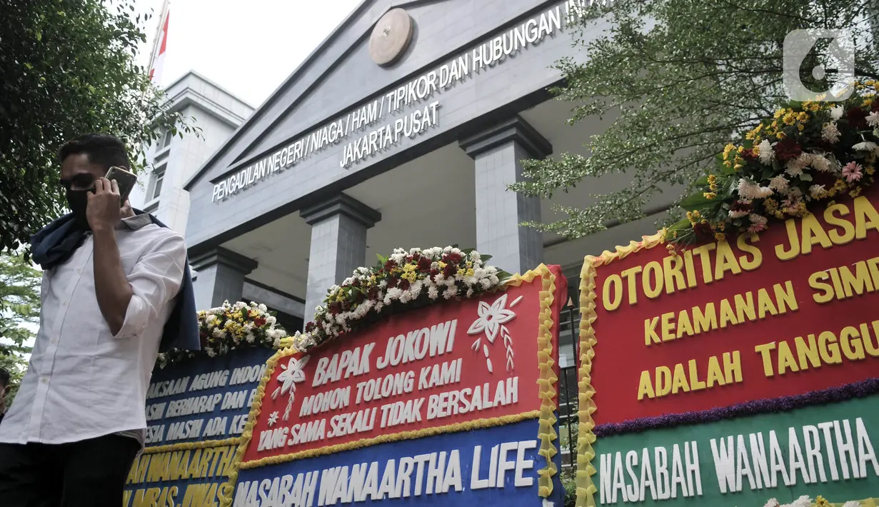 Warga menelepon dekat karangan bunga dari korban asuransi Jiwasraya yang terpajang di depan Gedung Pengadilan Tipikor, Jakarta, Rabu (3/6/2020). Puluhan karangan bunga tersebut berisi harapan para korban agar kasus segera tuntas dan uang mereka dapat kembali. (merdeka.com/Iqbal S. Nugroho)