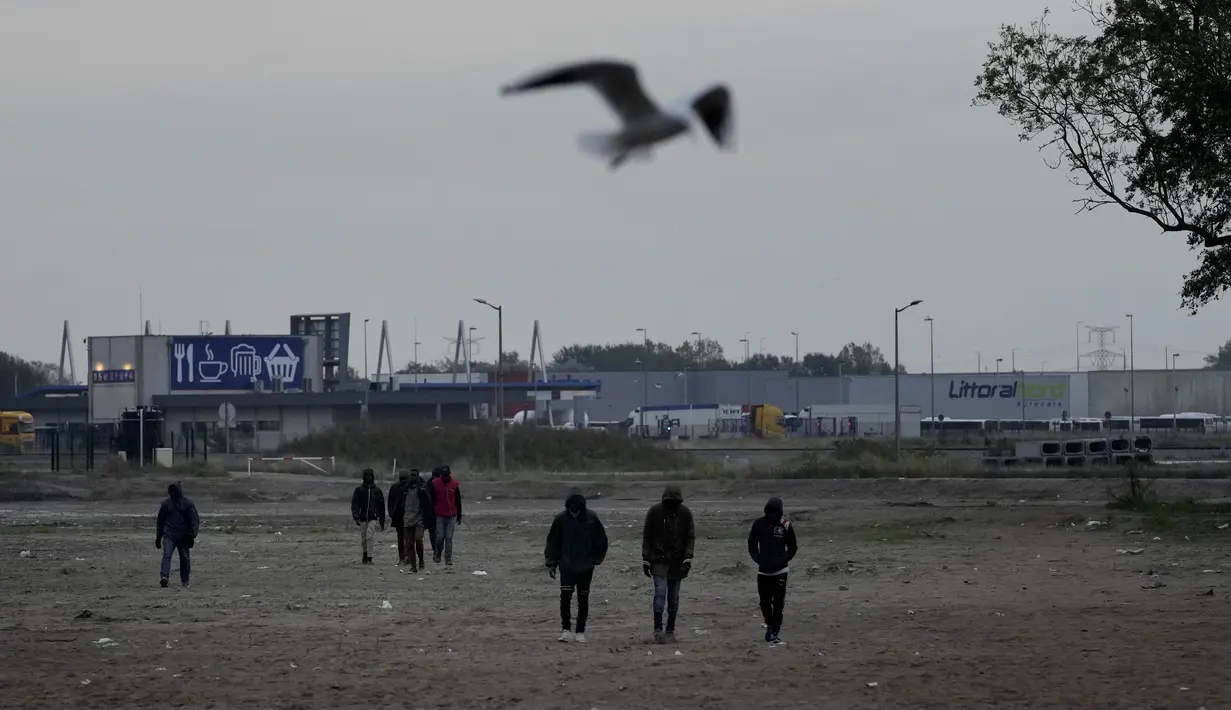 Para imigran berjalan di dekat sebuah kamp di Calais, Prancis pada 14 Oktober 2021. Dalam praktik berbahaya dan berpotensi mematikan, beberapa imigran mencoba melewati terowongan menuju Inggris yang dijaga ketat yang menghubungkan kedua negara dengan bersembunyi di truk. (AP/Christophe Ena)
