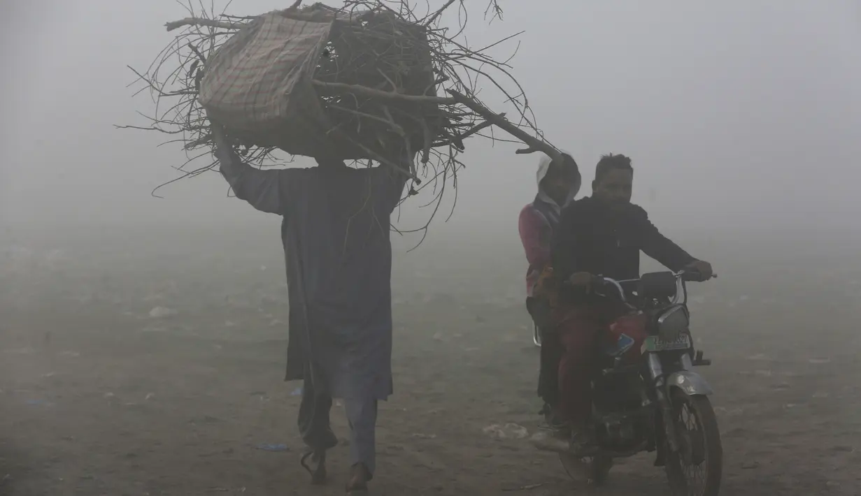 Seorang pria dan pengendara sepeda motor melintasi lapangan saat kabut tebal mengurangi jarak pandang di Lahore, Pakistan, Selasa (30/11/2021). Lahore secara konsisten menempati peringkat sebagai salah satu kota terburuk di dunia untuk polusi udara. (AP Photo/K.M. Chaudary)