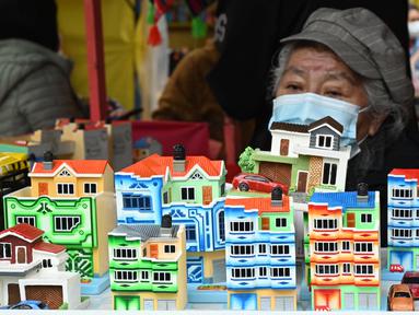Seorang perempuan menjual bangunan mini di kios pinggir jalan selama Alasitas Fair tahunan di La Paz, Bolivia pada 24 Januari 2022. Orang-orang membeli replika kecil dari barang-barang yang ingin mereka peroleh sepanjang tahun, seperti rumah, mobil, dan kekayaan. (AIZAR RALDES/AFP)
