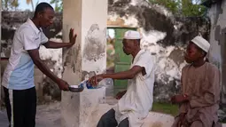 Pria Muslim berbagi sebotol air untuk berbuka puasa sebelum melaksanakan  salat magrib di desa Kumwamba, Pulau Ibo, 14 Mei 2019. Umat Islam di Mozambik melalui bulan Ramadan dengan badai yang menyebabkan sebagian besar masjid hancur dan persediaan makanan sangat terbatas (Zinyange Auntony/AFP)