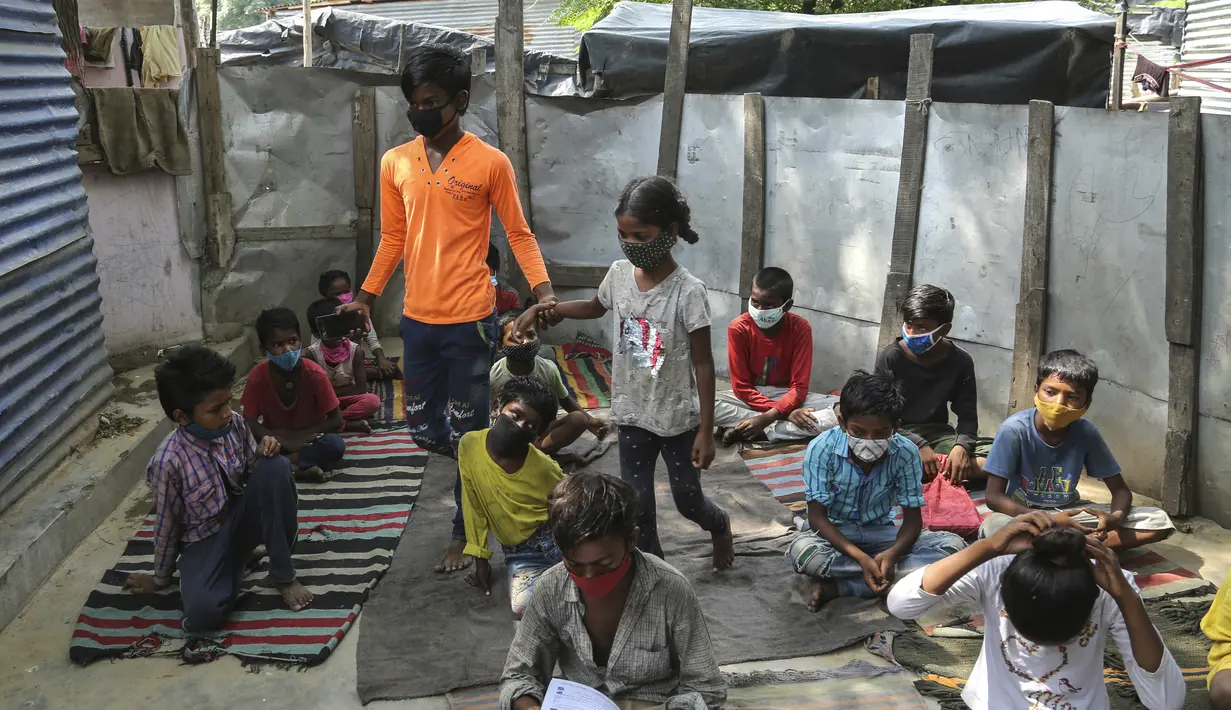 Seorang pemimpin siswa memimpin kelas ketika anak-anak mengenakan masker wajah sebagai tindakan pencegahan terhadap virus corona menghadiri kelas online di sebuah perkampungan kumuh di pinggiran Jammu, India, Senin, 14 Juni 2021. (AP Photo/Channi Anand)