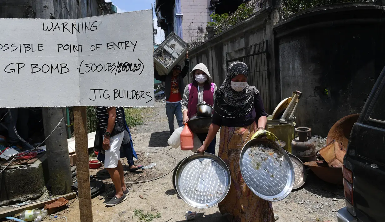 Warga membawa barang-barang yang dikumpulkan dari rumah mereka yang hancur saat pertama kali masuk ke Kota Marawi, Mindanao, Filipina, Minggu (1/4). Sebalumnnya, mereka mengungsi selama setahun terakhir akibat pertempuran di Kota Marawi. (TED ALJIBE/AFP)