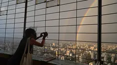 Seorang wanita mengambil foto pelangi ganda melalui pagar di Central Television Tower di Beijing (26/8/2021). Keindahan pelangi ganda dimanfaatkan warga Beijing untuk diabadikan lewat foto dan berfoto dengan latar pelangi itu. (AFP/Jade Gao)