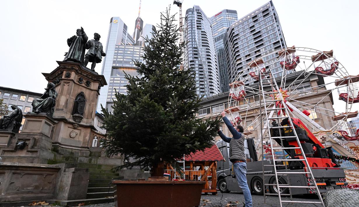 Seorang pria menghias pohon Natal di depan gedung pencakar langit salah satu distrik perbankan di pusat kota Frankfurt am Main, Jerman, pada tanggal 21 November 2024. (Kirill KUDRYAVTSEV/AFP)