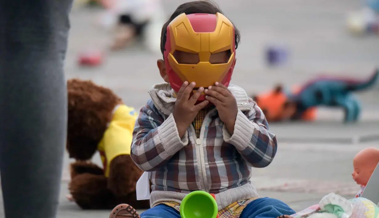 Seorang anak memakai topeng Iron Man saat ikut aksi di Alun-alun Bolivar, Bogota, Kolombia (20/11). Aksi ini memprotes penganiayaan terhadap anak sekaligus meningkatkan kesadaran akan tanggung jawab dalam perlindungan anak. (AFP Photo/Raul Arboleda)