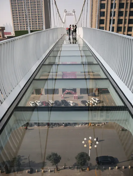 Sejumlah orang melintasi jembatan kaca di Shijiazhuang, Provinsi Hebei, China, Sabtu (24/11). Jembatan ini berdiri 30 meter di atas tanah. (AFP)