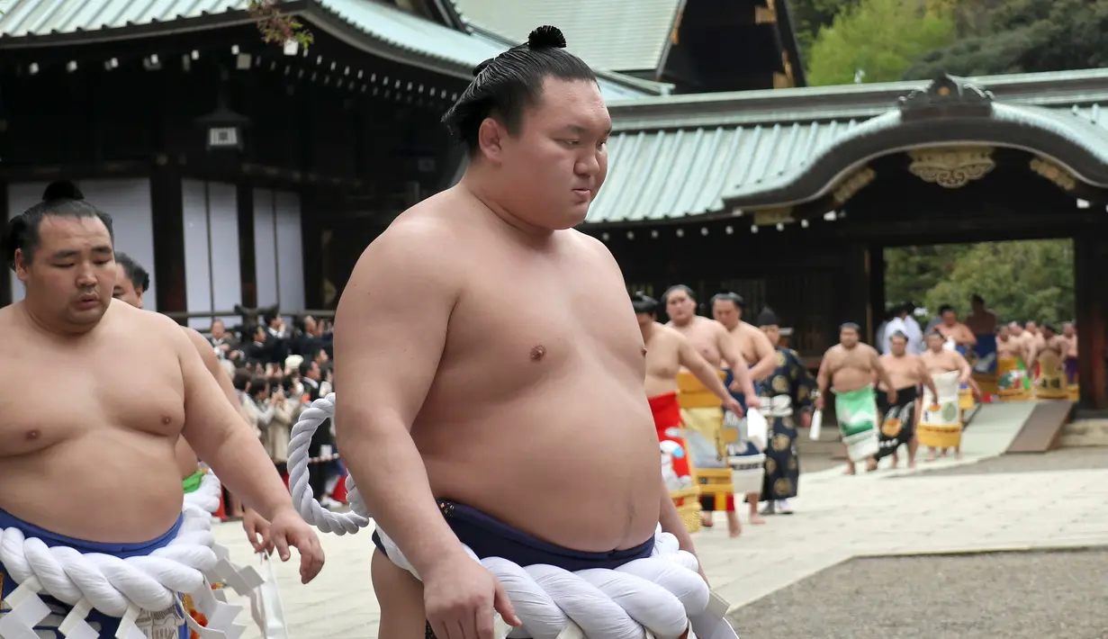 Pegulat sumo Hakuho (depan) dan Kakuryu (kiri) dari Mongolia berjalan dengan para pegulat sumo lainnya setelah berdoa di Kuil Yasukuni di Tokyo, Jepang, Senin (17/4). (AP Photo / Shizuo Kambayashi)