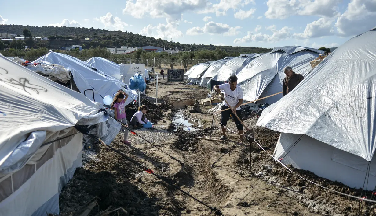 Para migran menggali di sekitar tenda setelah hujan badai di kamp pengungsi Kara Tepe, di pulau Lesbos, Yunani (14/10/2020).  Sekitar 7.600 pengungsi dan migran telah menetap di kota tenda baru setelah kebakaran berturut-turut pada tanggal 14 September. (AP Photo/Panagiotis Balaskas)