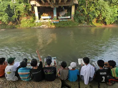 Anak-anak menunggu berbuka puasa dengan membaca buku di Saung Pustaka Air di Depok, Jawa Barat, (30/5). Perpustakaan ini menjadi sarana edukasi untuk menjaga dan mengenalkan area konservasi keanekaragaman hayati. (Liputan6.com/Herman Zakharia)