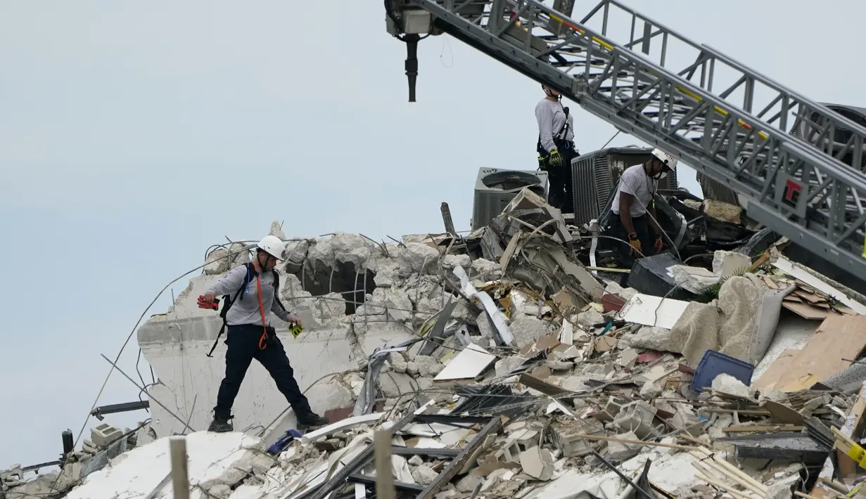 Tim penyelamat berjalan di antara puing-puing dari sebagian menara apartemen tepi laut yang runtuh di Surfside, utara Miami, Kamis (24/6/2021). Runtuhnya gedung apartemen setinggi 12 lantai tersebut mengakibatkan satu orang tewas dan puluhan lainnya masih dinyatakan hilang. (AP Photo/Lynne Sladky)