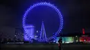 Pejalan kaki melintas di depan London Eye yang diterangi dengan cahaay biru untuk berterima kasih kepada National Health Service (NHS) di London, Kamis (7/1/2021). NHS merupakan sistem layanan kesehatan nasional yang menjadi ujung tombak Inggris dalam memerangi pandemi Covid-19. (Tolga Akmen / AFP)