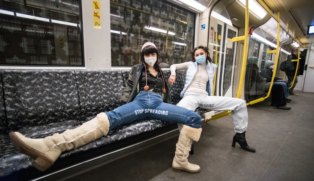 Elena Buscaino (kanan) dan Mina Bonakdar berpose dengan Riot Pants bertuliskan "Stop Spreading" di kereta bawah tanah di Berlin, 5 Februari 2021. Aktivis feminis itu dalam misi menghentikan kebiasaan penumpang pria melebarkan kaki saat duduk sehingga memakan dua kursi kereta. (STEFANIE LOOS/AFP)