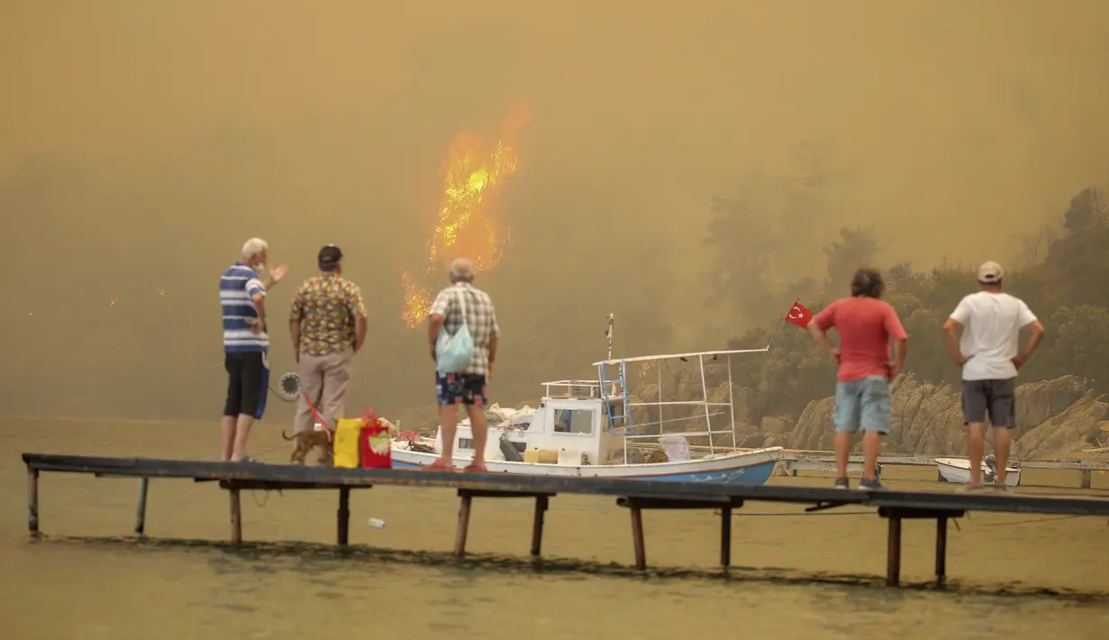 Turis menunggu untuk dievakuasi dari daerah Mazi yang diselimuti asap saat kebakaran hutan berguling menuruni bukit menuju pantai di Bodrum, Mugla, Turki, Minggu (1/8/2021). Menurut para pejabat, lebih dari 100 kebakaran hutan telah dikendalikan di Turki. (AP Photo/Emre Tazegul)