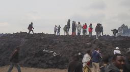 Orang-orang berkumpul di aliran batu lava dingin setelah letusan Gunung Nyiragongo di Goma, Kongo (23/5/2021). Saksi mata mengatakan Gunung Nyiragongo mengeluarkan lahar yang menghancurkan rumah-rumah berpenduduk hampir 2 orang juta sebagian besar terhindar setelah letusan. (AP Photo/Justin Kabumba)