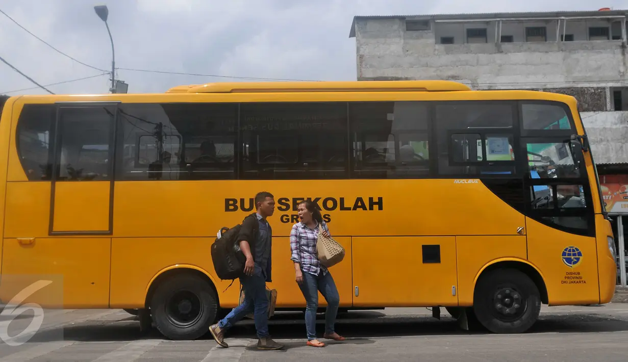 Dua orang warga melintas di depan Bus Sekolah di Terminal Senen, Jakarta, Senin (21/12/2015). Bus sekolah menggantikan Metro Mini yang melakukan aksi mogok karena takut terkena razia Dishub. (Liputan6.com/Gempur M Surya)