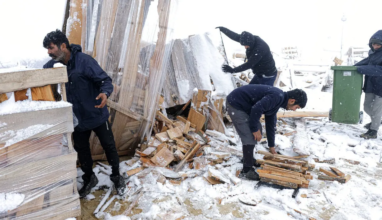 Para imigran mengumpulkan kayu bakar ke dalam tempat sampah di Kamp Lipa, luar Bihac, Bosnia, Jumat (8/1/2021). Cuaca bersalju dan musim dingin telah membawa lebih banyak penderitaan bagi ratusan imigran yang terjebak selama berhari-hari di kamp tersebut. (AP Photo/Kemal Softic)