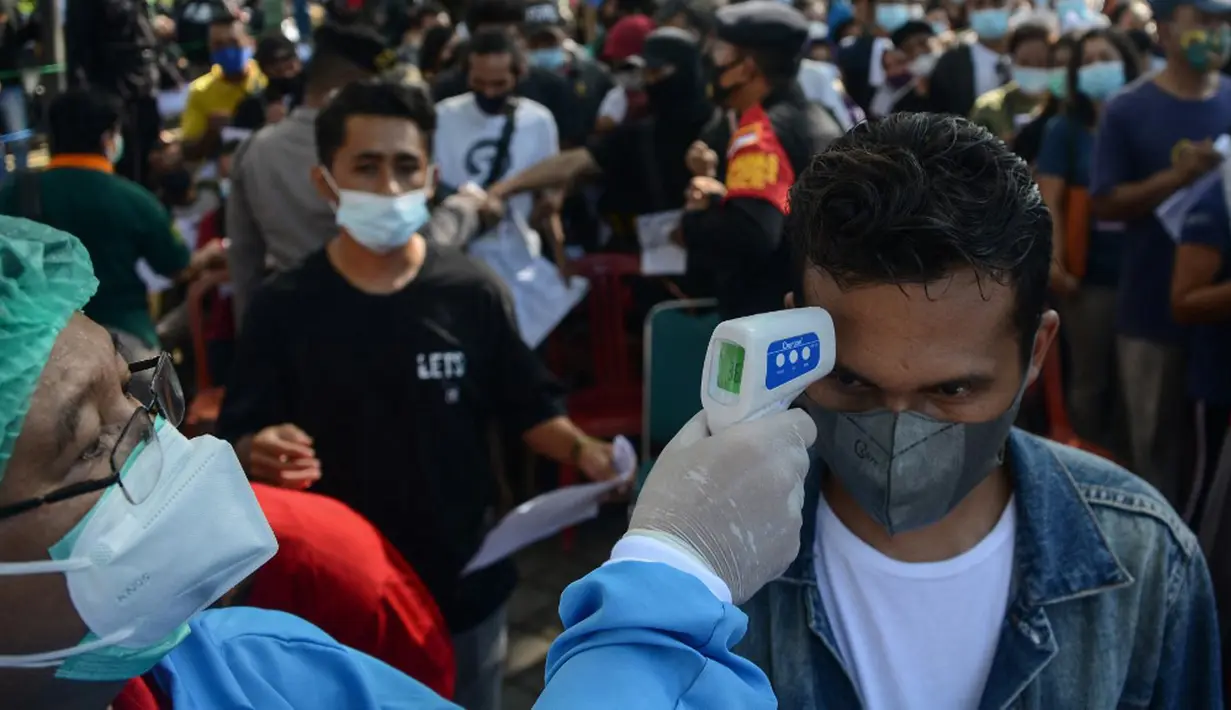 Petugas memeriksa suhu tubuh warga yang mengikuti vaksinasi virus corona COVID-19 AstraZeneca di Denpasar, Bali, Sabtu (26/6/2021). Ratusan warga terlihat antusias mengikuti vaksinasi massal tersebut. (SONY TUMBELAKA/AFP)