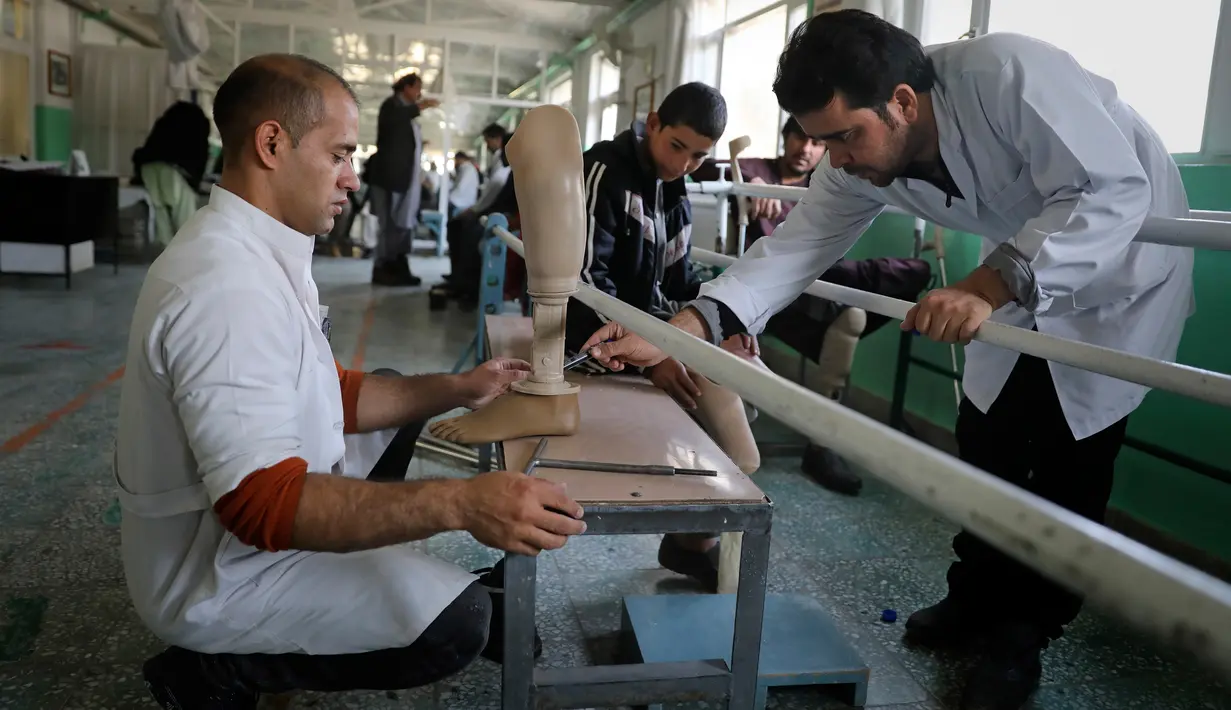 Staf ortopedi menyesuaikan prothesis untuk Abdullah (13) yang kehilangan kaki kirinya saat menginjak improvised explosive device (IED) di pusat rehabilitasi fisik Komite Internasional Palang Merah (ICRC), Kabul, Afghanistan, Minggu (1/12/2019). (AP Photo/Altaf Qadri)