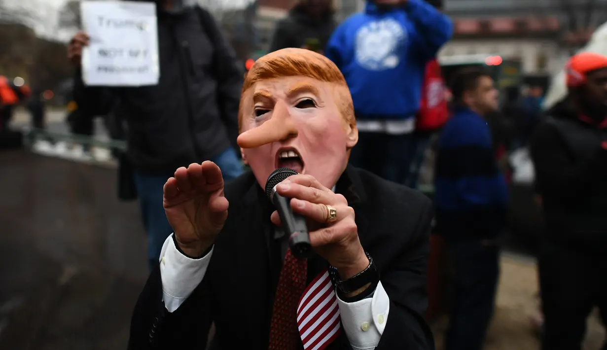 Aksi penolakan Donald Trump sebagai Presiden AS di Washington DC, Jumat (20/1). Seorang demonstran memakai topeng berwajah mirip Trump dengan hidung yang dipanjangkan. (AFP PHOTO / Jewel SAMAD)