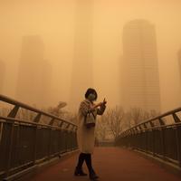 Seorang perempuan berjalan di sepanjang jembatan penyeberangan di tengah badai pasir pada jam sibuk pagi hari di kawasan pusat bisnis di Beijing, China, Senin (15/3/2021). Kota Beijing diselimuti debu cokelat tebal, Senin pagi, yang dibawa angin kencang dari Mongolia. (AP Photo/Mark Schiefelbein)