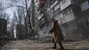 Seorang wanita berjalan melewati gedung apartemen yang terbakar setelah penembakan di Mariupol, Ukraina, Minggu, 13 Maret 2022. Pada 24 Februari 2022, Rusia melancarkan invasi berskala besar ke Ukraina, salah satu negara tetangganya di sebelah barat daya. (AP Photo/Evgeniy Maloletka)
