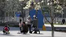 Warga yang mengenakan masker membawa anak-anak mereka berjemur di luar kompleks perumahan di Beijing, Minggu (3/4/2022). Kasus COVID-19 di kota terbesar di China, Shanghai, masih meningkat saat jutaan orang tetap terisolasi di rumah di bawah lockdown besar-besaran. (AP Photo/Andy Wong)