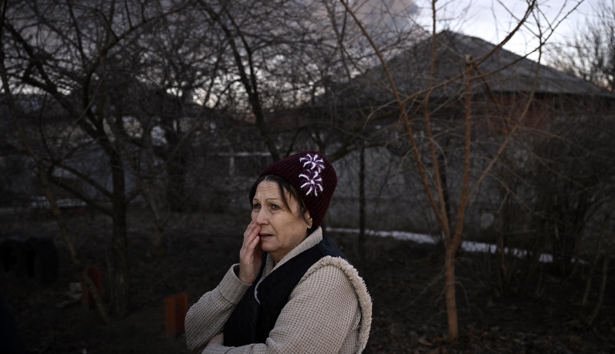 Seorang wanita berdiri di jalan saat asap hitam mengepul dari bandara militer di Chuguyev, dekat Kharkiv, 24 Februari 2022. Presiden Rusia Vladimir Putin mengumumkan operasi militer di Ukraina. (Aris Messinis/AFP)