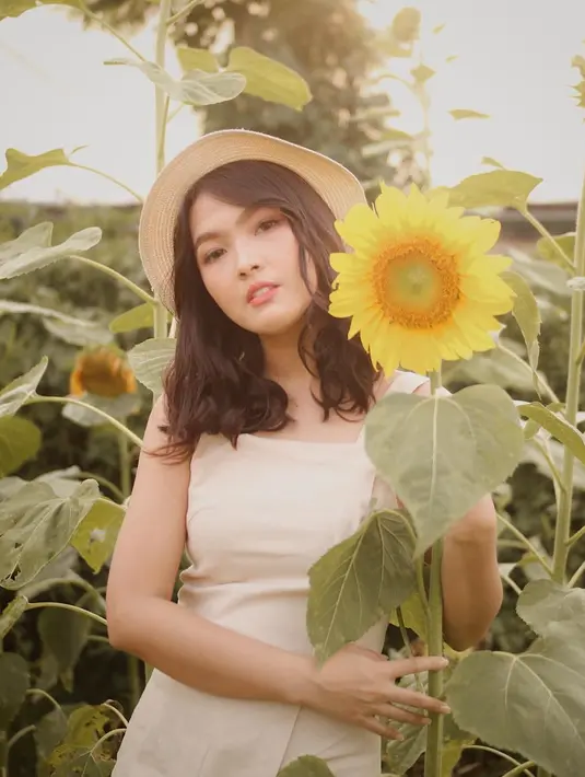 Pergi berlibur berkunjung ke taman bunga matahari, Ana memilih baju tanpa lengan bewarna putih. Dipadukan dengan topi rotan, penampilan liburan ala pemeran Rinjani ini semakin kece. (Liputan6.com/IG/@anariana27)