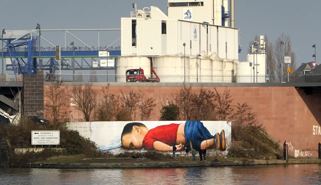 Pembuat grafiti, Justus Becker dan Oguz Sen melukis mural bergambar Aylan Kurdi, bocah Suriah yang jasadnya ditemukan di pantai barat daya Turki pada September 2015, di sebuah tembok di sungai Main, Frankfurt, Jerman, 10 Maret 2016. (Daniel ROLAND/AFP)