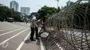 Anggota polisi merapihkan kawat berduri yang dipasang di depan Istana Negara, Jakarta pada peringatan May Day, Senin (1/5). Istana Negara menjadi titik konsentrasi puluhan ribu buruh yang memperingati Hari Buruh Internasional (Liputan6.com/Gempur M Surya)