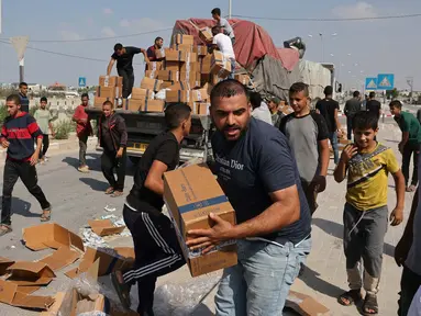 Orang-orang membongkar kotak-kotak bantuan kemanusiaan dari sebuah truk yang memasuki Jalur Gaza Selatan dari Mesir melalui penyeberangan perbatasan Rafah pada 2 November 2023. (MOHAMMED ABED/AFP)