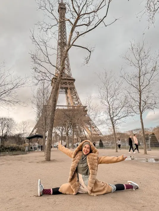 Berpose di depan menara Eiffel, Ria Ricis tampil kece memadukan gamis dan hijab nuansa hijau sage-nya dengan long coat warna coklat muda. [@riaricis1795]