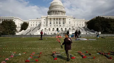 Seorang wanita meletakkan bunga di halaman rumput Gedung Capitol (kantor kongres) Amerika Serikat, Senin (19/3). 5000 bunga diletakkan untuk mengenang ribuan anak yang tewas akibat pengeboman oleh koalisi pimpinan Arab Saudi di Yaman (AP/Jacquelyn Martin)