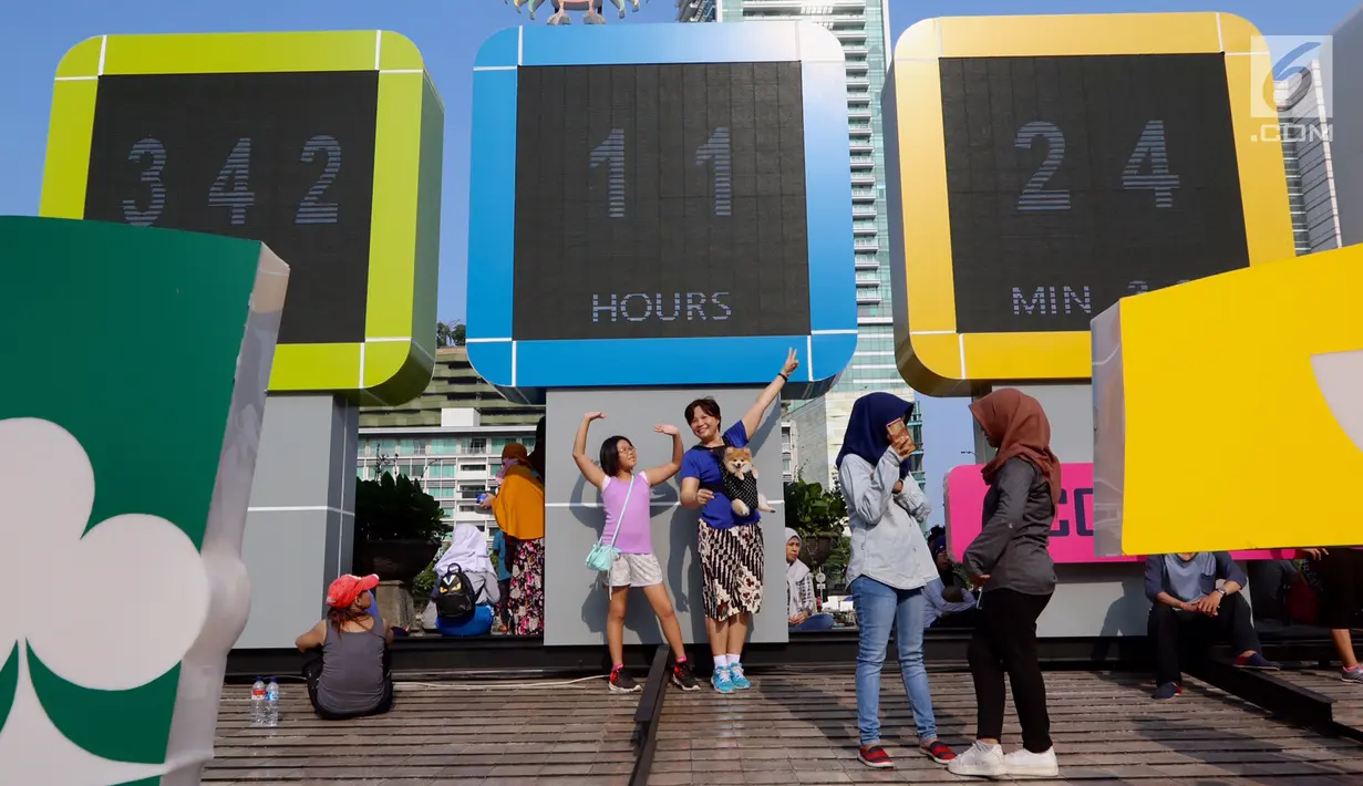 Seorang ibu dan anaknya di foto dengan latar layar Countdown Asian Games 2018 saat Car Free Day di Bundaran HI, Jakarta, Minggu, (10/09). (Liputan6.com/Fery Pradolo)
