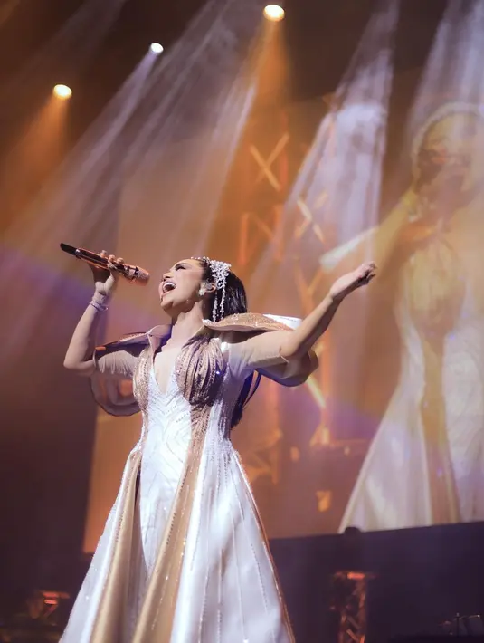 Untuk konser tunggalnya ini, Krisdayanti mengenakan gaun dengan detail tambahan cape di bagian pundak. Gaun dua warna putih-cokelat ini tampak sempurna membalut tubuhnya bak seorang ratu. Foto: Instagram.