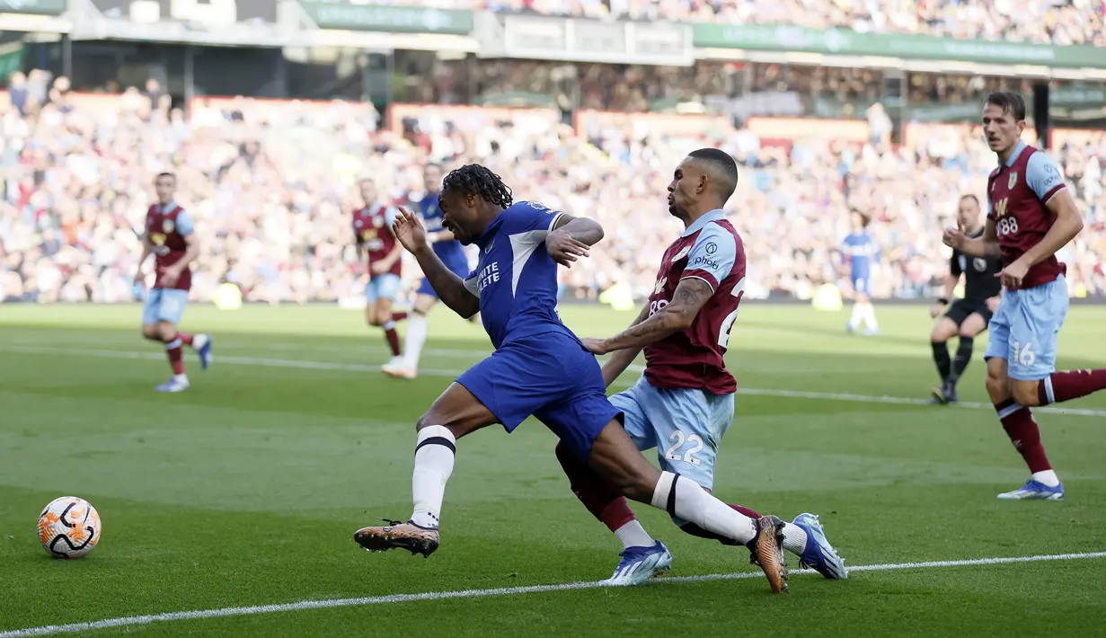 Pemain Chelsea, Raheem Sterling, terjatuh saat berusaha melewati pemain Burnley, Vitinho, pada laga pekan ke-8 Premier League 2023/2024 di Stadion Turf Moor, Sabtu, (7/10/2023). Pemain asal Inggris itu tampil luar biasa. Dia terlibat dalam semua gol The Blues di pertandingan tersebut. (Richard Sellers/PA via AP)