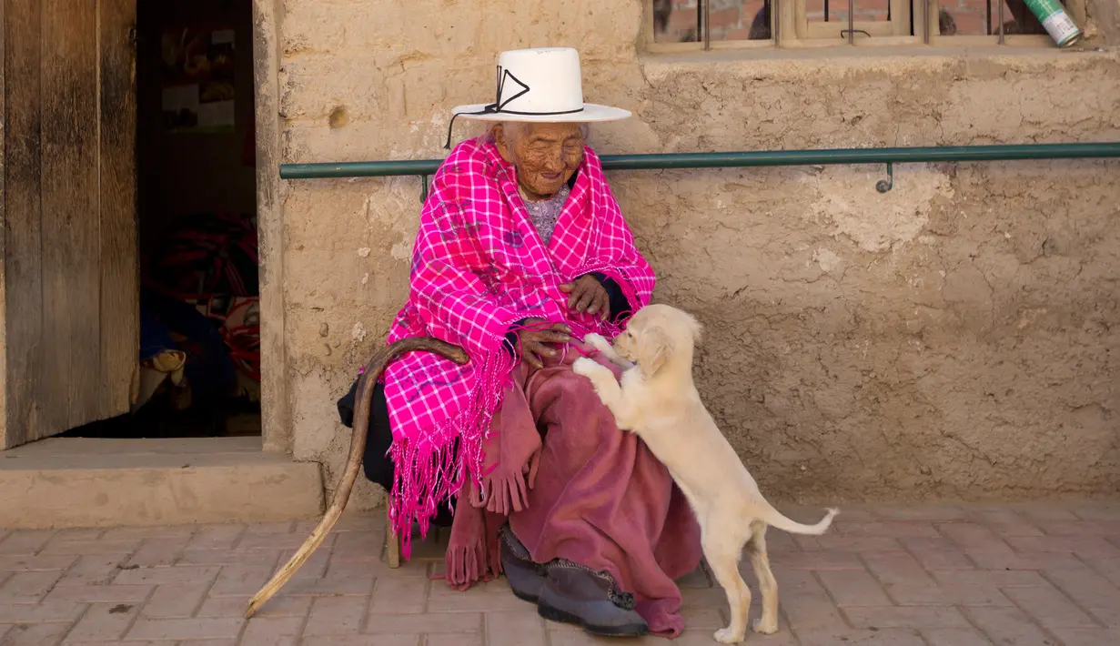 Julia Flores Colque bermain dengan salah satu anjing peliharaan keluarga di luar rumahnya di Sacaba, Bolivia, 23 Agustus 2018. Namun sayang, museum Guinness World Records belum berencana memasukkan nama Julia sebagai manusia tertua. (AP/Juan Karita)